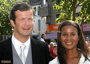 Prince Maximilian and Princess Angela of Liechtenstein are smiling. Prince Maximilian is wearing a white long sleeve under a light gray striped necktie, gray vest, and black coat while Princess Angela is wearing a white blouse and earrings