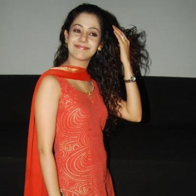 Karishma Randhawa as Princess Dollie Suri, with a tight-lipped smile and curly hair while wearing an orange sleeveless dress