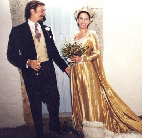 Princess Olga wearing a yellow gown and holding a bouquet of flowers and Prince Aimone wearing a black suit and holding a wine glass.