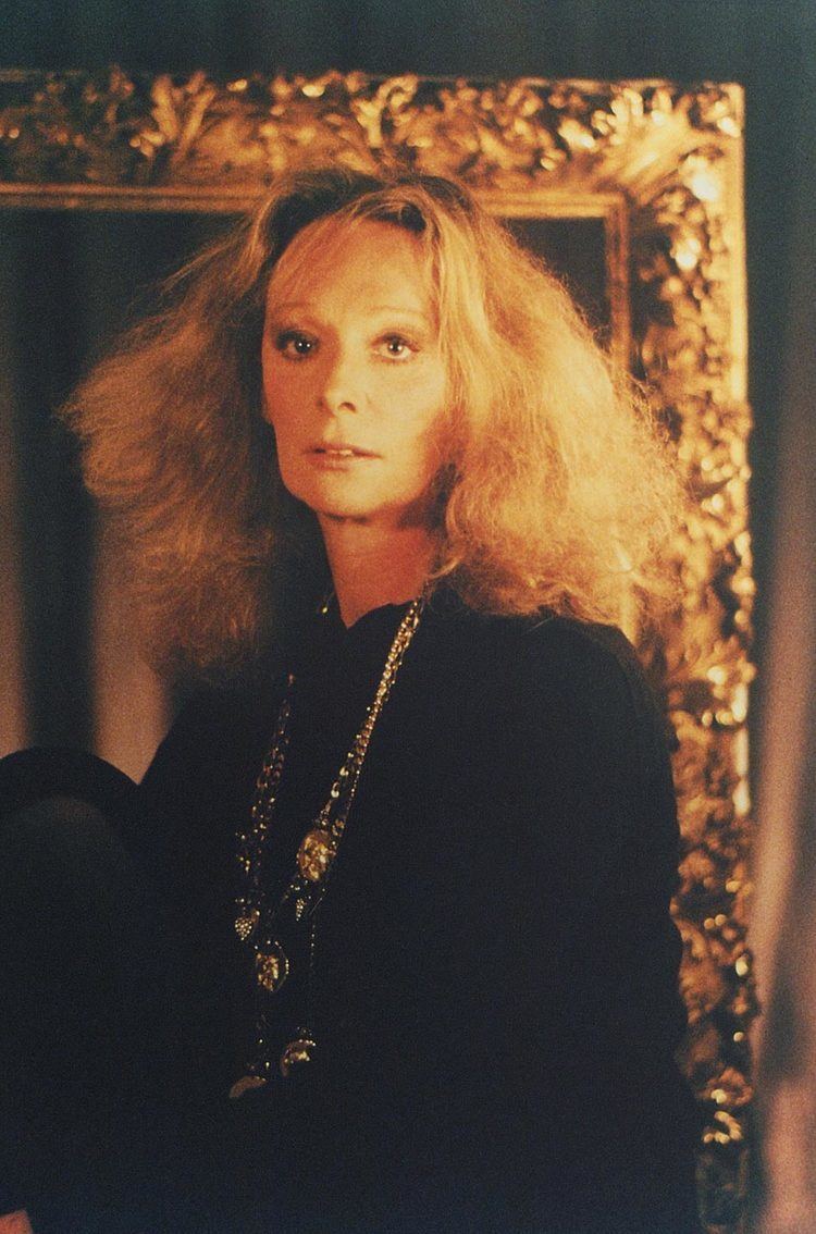 Princess Stephanie of Windisch-Graetz with a serious face, curly blonde hair, wearing a necklace and a black long sleeve dress.