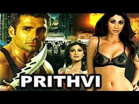 The movie poster of Prithvi 1997, In front is the movie title PRITHVI. At the back is a city building, cars and fire, On the left side, Suniel Shetty is serious, holding a combat knife, has black hair shaved beard and mustache wearing a gold necklace and black tank top, in the middle, Shilpa Shetty is smiling, standing, left hand palm open, has brown hair, wearing earrings, silver rings, and silver bracelet and red dress. On the right side, Shilpa Shetty is smiling, standing, left hand on her waist, has long black hair, wearing a black lingerie.