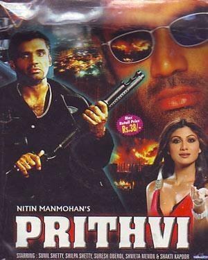 In the movie poster of Prithvi 1997,In front is the movie title Nitin Manmohan’s Prithvi. on the left side, Suniel Shetty is serious, standing, holding a shotgun trigger with his right hand and left arm on his forearm, has black hair, shaved mustache, and beard, wearing a black shirt and black coat, at the back is a burning city, at the top right side, Suniel Shetty is serious, has black hair, shaved beard and mustache, wearing silver shades. At the bottom right side, Shilpa Shetty is smiling, standing, left-hand palm open, has brown hair, wearing earrings, silver rings, a silver bracelet on her left hand, and a red dress. In front is the movie title Nitin Manmohan’s Prithvi.