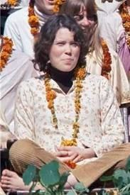 Prudence Farrow smiling while sitting on the floor and wearing a floral blouse and garland