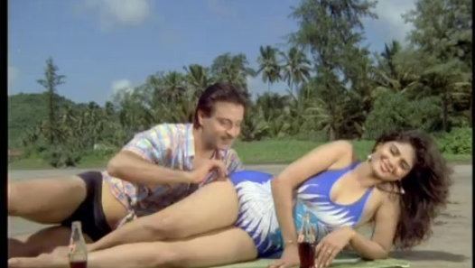 Deepak Parashar and Amita Nangiav are smiling while lying on the sand in a movie scene from Purani Haveli, a 1989 Indian Hindi-language horror film.