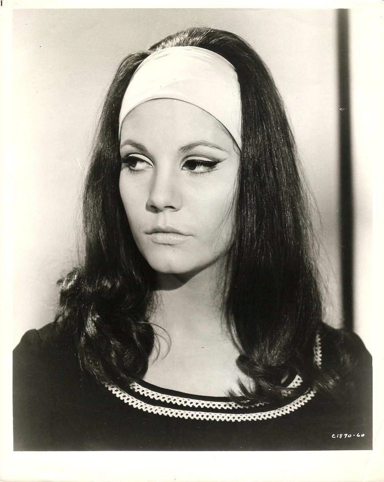 Quentin Dean with long wavy hair, wearing a white headband and a black shirt.