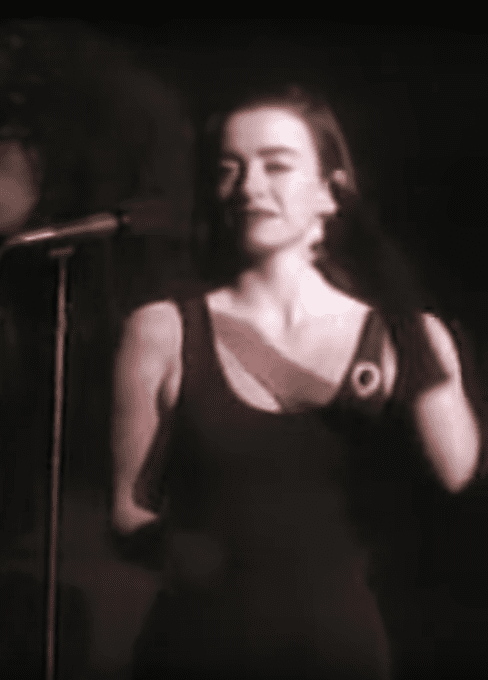 Rachel Fury singing while wearing a black sleeveless dress, black gloves, and earrings
