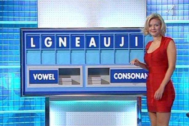 On Countdown, Rachel Riley is smiling and has short blonde hair, her right hand up, a background of blue tiles, has a board on her side, with the letter “L, G, N, E, A, U, J, I” a vowel word on the bottom left with piled tile letters and consonant on the bottom right with piled tile letters, she is wearing a red dress.