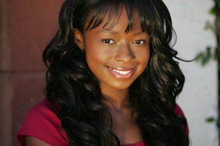 Rae'Ven Larrymore Kelly smiling with black curly hair while wearing a red blouse