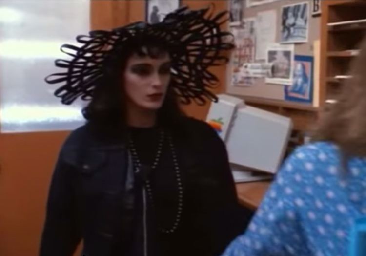 Rainbow Harvest wearing a black hat and black leather jacket in a movie scene from the 1990 film Mirror Mirror
