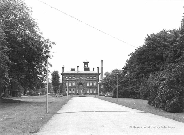 A Black and White front view of the Rainhill Hospital with visible lampposts and trees along the pathway.