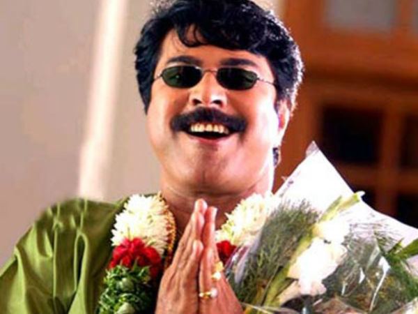 Mammootty with a mustache and a smiling face while holding flowers, wearing sunglasses, rings, and a green shirt.