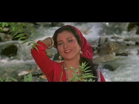 In the movie scene of  Ram Teri Ganga Maili 1985, Mandakini is smiling, standing in the middle with a river behind her, posing with her right hand up behind her head,  has black hair brown eyes wearing a nose piercing, gold earrings, gold necklace, gold bracelets on her right hand, red cloth over her head and red checkered long sleeve dress.