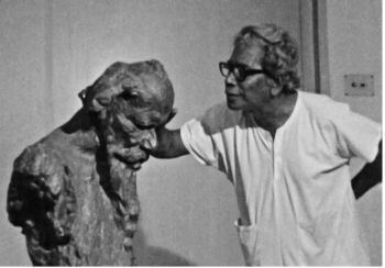 Ramkinkar Baij carving a sculpture nd wearing a white shirt and eyeglasses