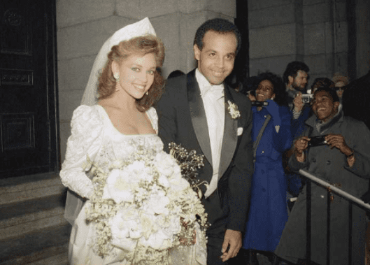 Vanessa Williams smiling and wearing a white gown while Ramon Hervey wearing a black coat and white long sleeves on their wedding day