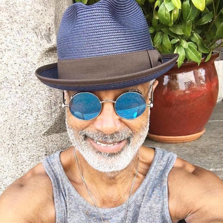 Ramon Hervey II smiling while wearing a blue hat, blue shades, gray sando and necklace