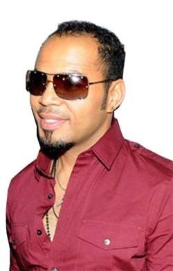 Ramsey Nouah smiling and wearing maroon long sleeves, necklace, and shades