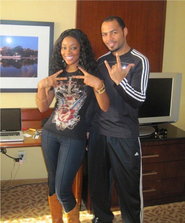 Ramsey Nouah smiling with his wife Emelia Philips-Nouah wearing a black printed shirt, jeans, and brown boots