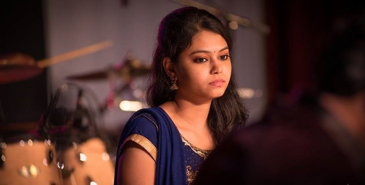 Ramya Behara with a serious face, wearing earrings, and a blue Indian dress.