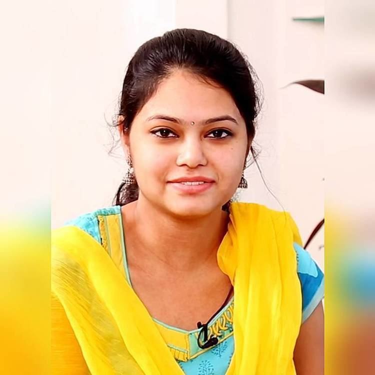 Ramya Behara smiling, wearing earrings, a yellow scarf, and a light blue Indian dress.