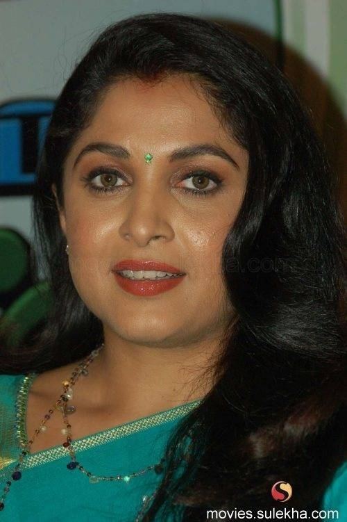 Ramya Krishnan smiling while wearing a green and blue dress, beaded necklace, and earrings