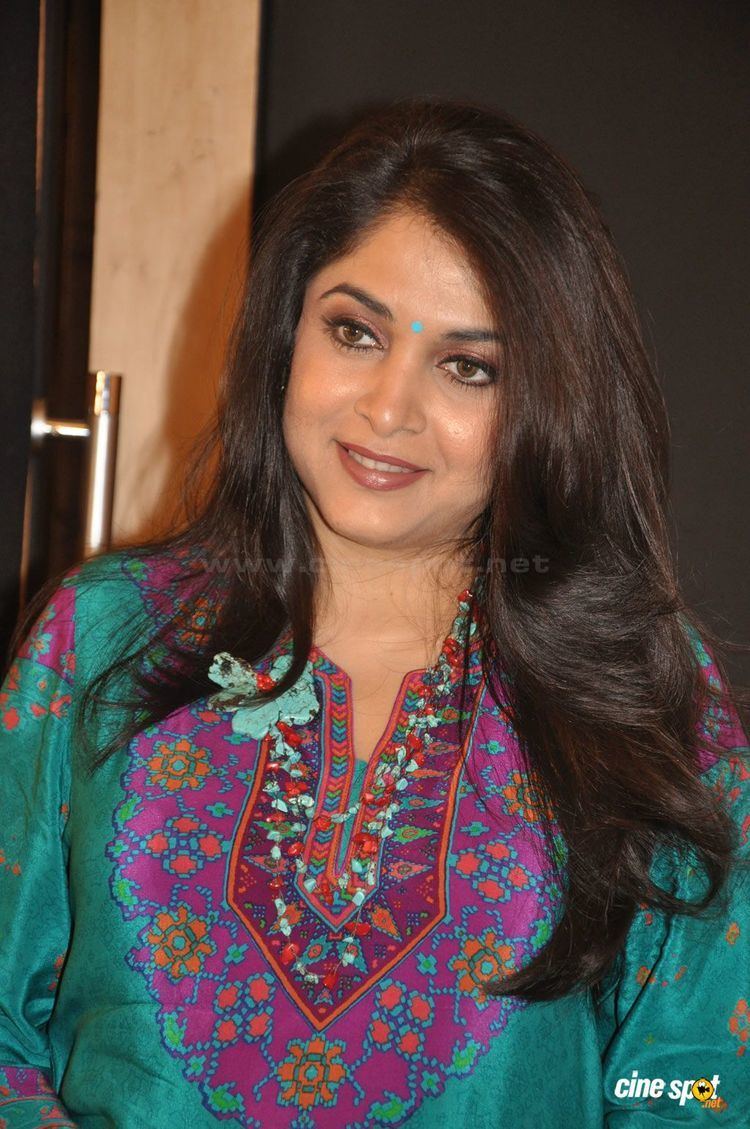 Ramya Krishnan smiling while wearing a blue-green, purple, and orange dress