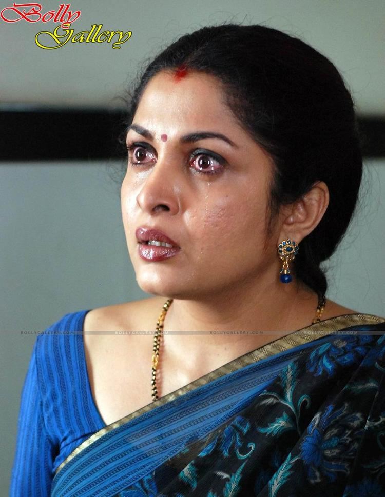 Ramya Krishnan crying while wearing a blue dress, black and blue dupatta, beaded necklace, and blue earrings