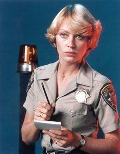 Randi Oakes wearing uniform of a police officer while holding a pen and paper