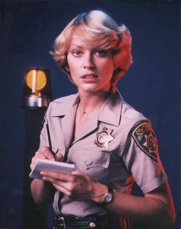 Randi Oakes wearing uniform of a police officer while holding a pen and paper