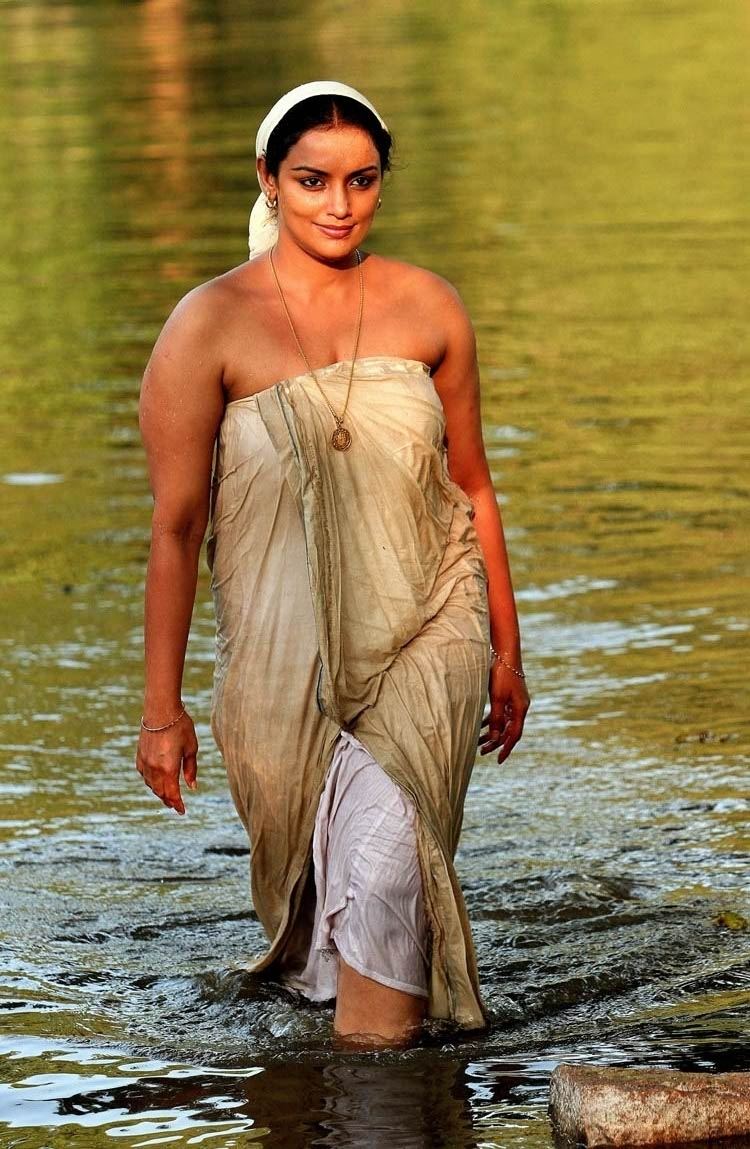 Shweta Menon smiling while walking in the lake and wearing a beige dress and bandana in a movie scene from the 2011 film Rathinirvedam