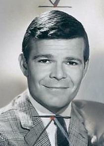 Young Ray Fulmer smiling and wearing checkered coat, long sleeves and neck tie