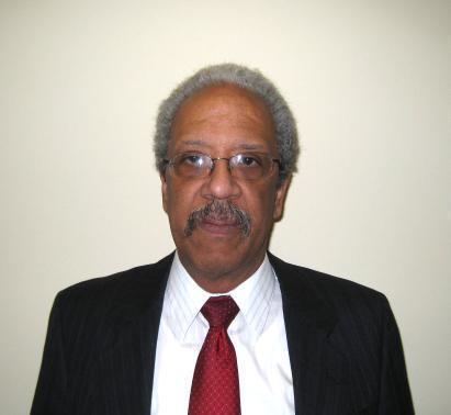 Raymond P. Moore with mustache while wearing eyeglasses, black coat, white long sleeves, and red necktie