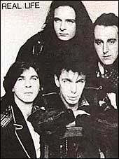 Poster of Real Life band featuring its members. Alan Johnson, Danny Simcic, Richard Zatorski, and David Sterry with serious faces and wearing black jackets.