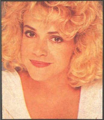 Rebeca Arthur with a tight-lipped smile and blonde curly hair while wearing a white blouse