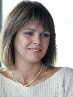 Rebecca Gilling smiling, with short blonde hair, wearing a necklace and a white knitted shirt.