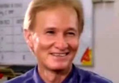 Redford White smiling while looking at something and wearing a blue collared shirt.