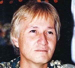 Redford White smiling while looking at something and wearing a floral polo shirt.