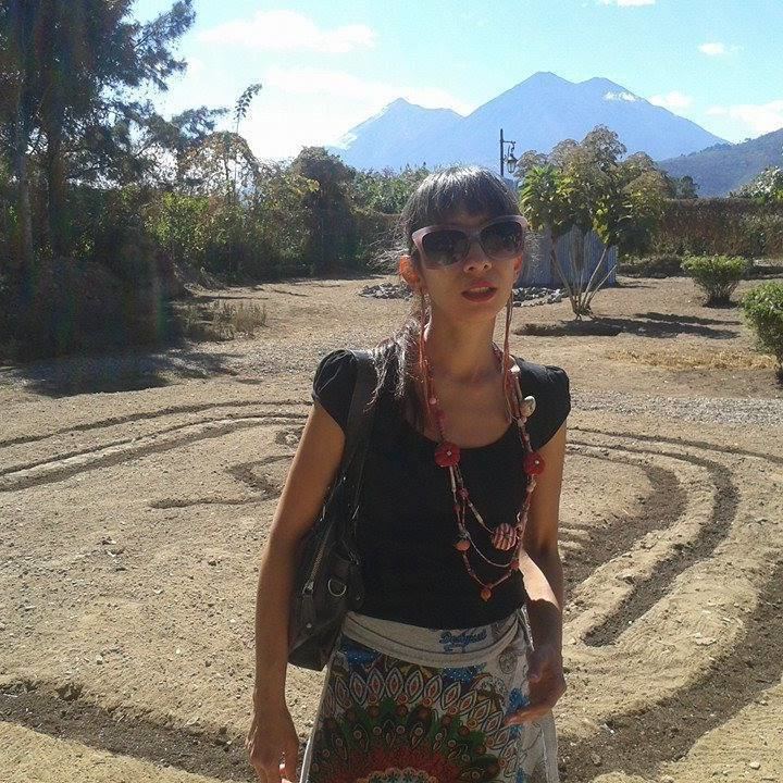 Regina José Galindo with a serious face while carrying a black bag, wearing sunglasses, a necklace, a black shirt, and a multi-colored skirt.