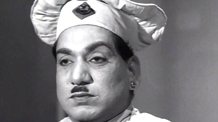 A black and white photo of Relangi Venkata Ramaiah with a serious face and a mustache, wearing a chef hat and earrings.