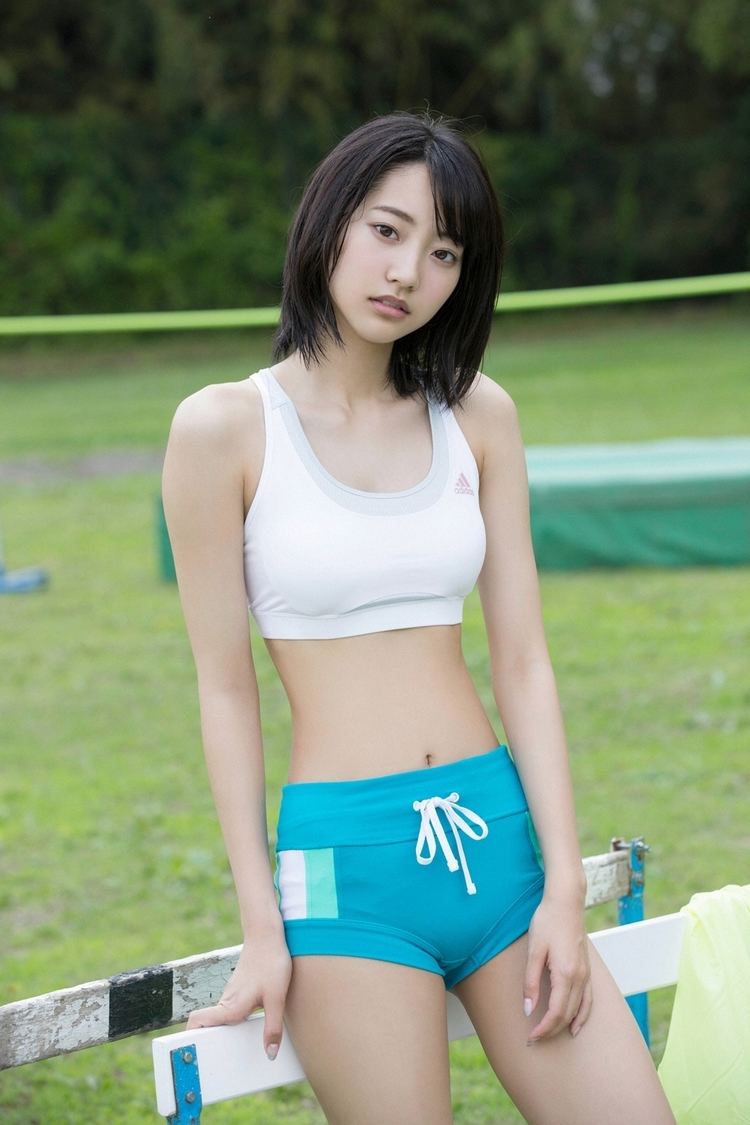 Rena Takeda with a serious face while leaning on a fence, with black short hair, wearing a white sports bra and turquoise shorts.