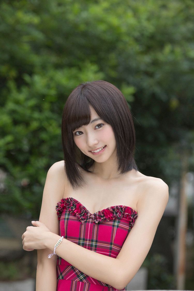 Rena Takeda smiling while holding her arm, with short hair, and wearing a red checkered tube dress.