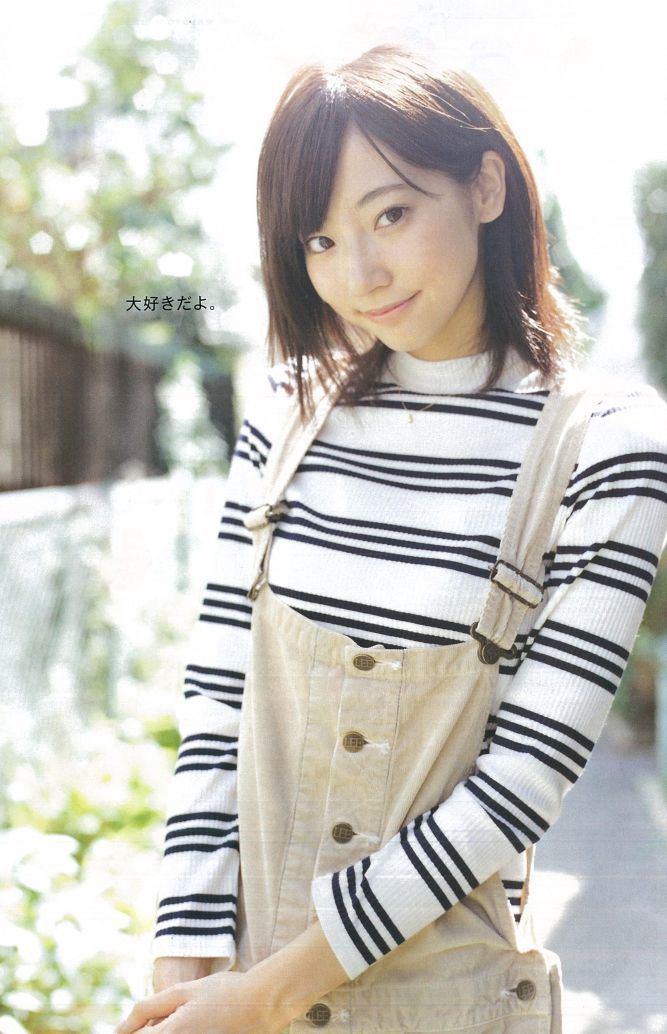 Rena Takeda smiling, with short hair, and wearing a light brown jumper over a white and black long sleeve shirt.
