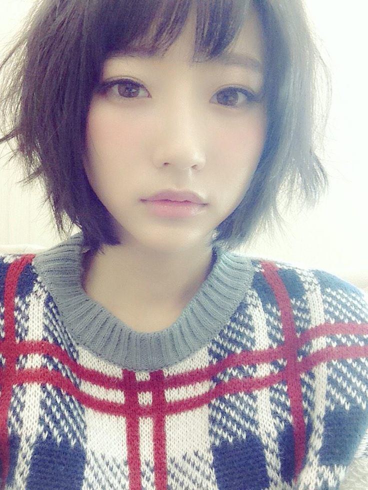 Rena Takeda with a serious face, messy short hair, and wearing a multi-colored knitted sweatshirt.