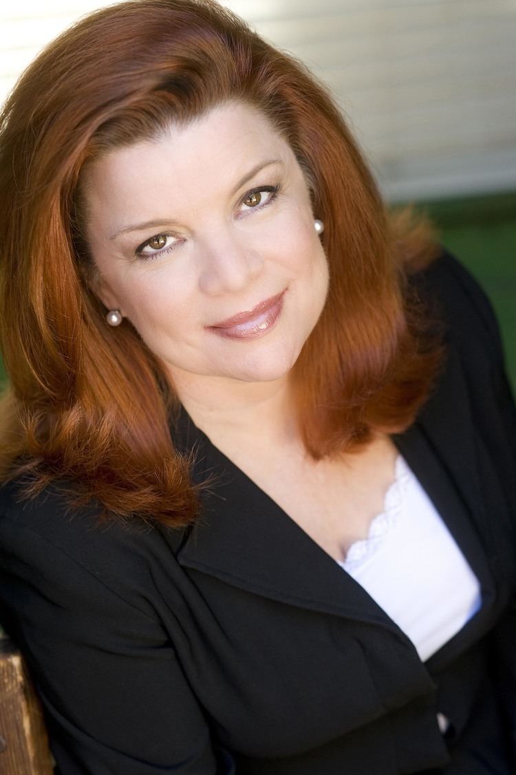 Renee Lawless in her tight lipped smile while wearing black coat and white inner top