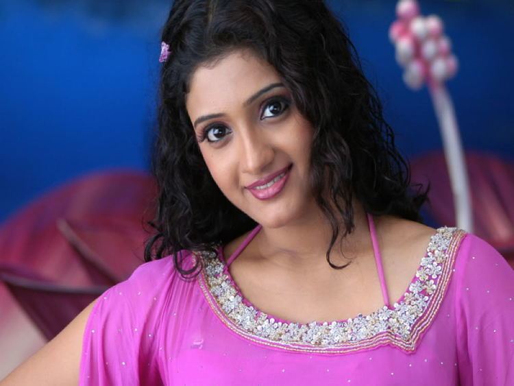 Renuka Menon smiling while wearing a violet beaded blouse and hair clip