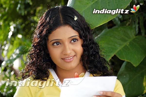 Renuka Menon smiling while holding a piece of paper and wearing a white and yellow blouse and hair clip