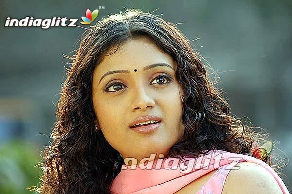 Renuka Menon with a shocked face and curly hair while wearing a pink scarf and pink blouse