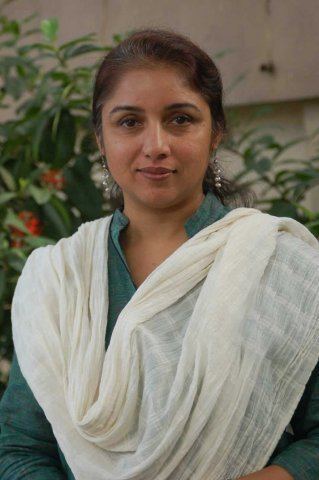 Revathi's tight lipped smile while wearing blue green dress and white shawl