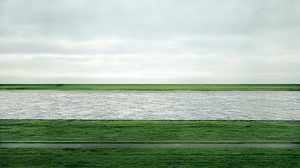 A river flows horizontally across the field between flat green fields under an overcast sky.