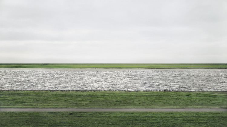 A river flows horizontally across the field between flat green fields under an overcast sky.