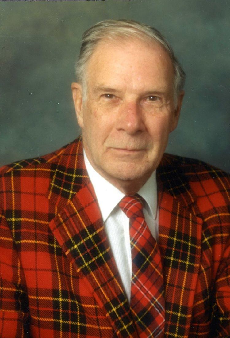 Richard Hamming with a tight-lipped smile while wearing a black and red checkered coat, white long sleeves, and checkered necktie